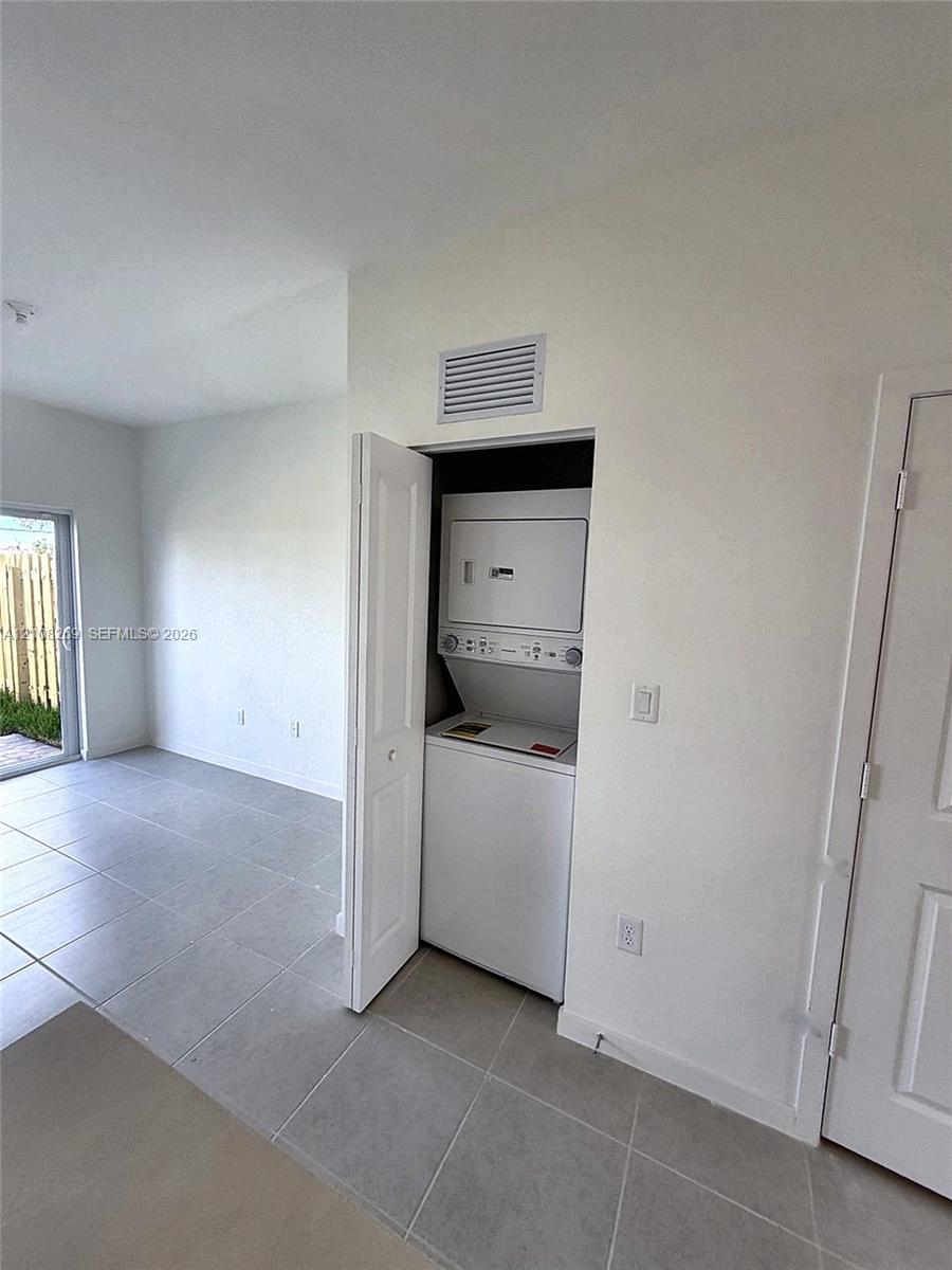 Closet-housed stacked laundry unit with ceramic tile flooring and neutral-toned wall finishes