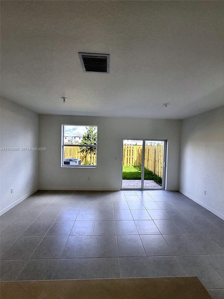 Open-concept interior featuring large-format ceramic tile flooring, neutral walls, a single-hung window, and a sliding glass door providing external access