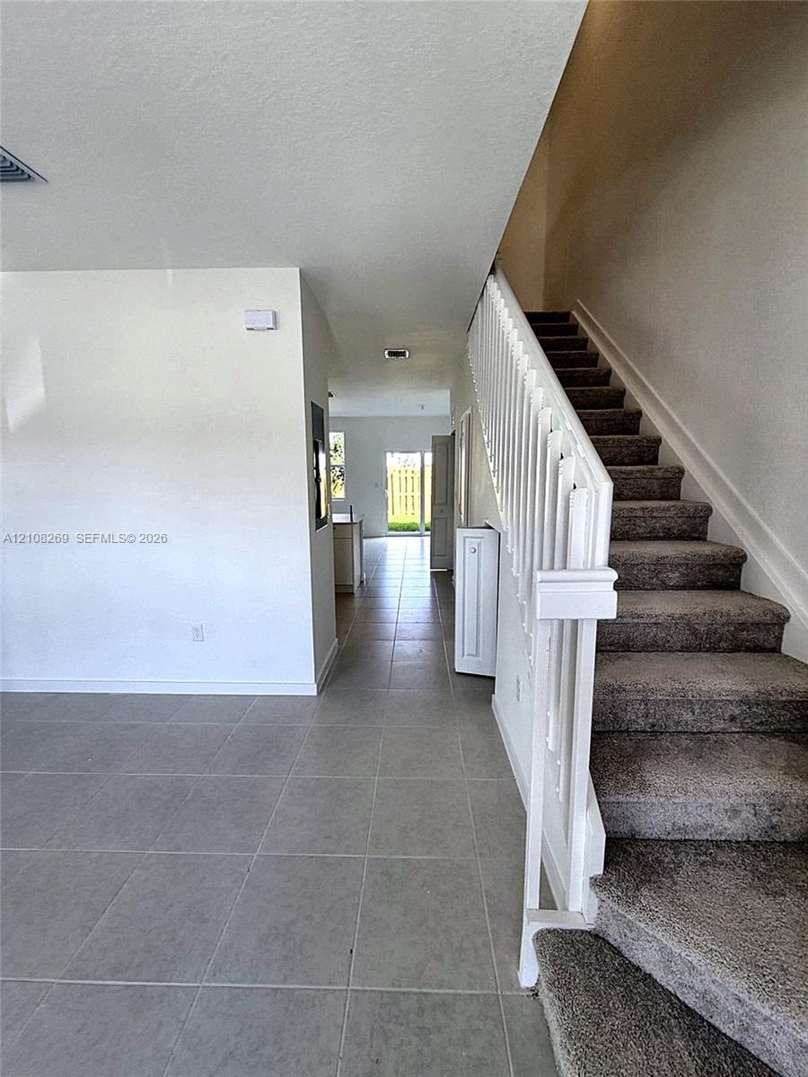 Large-format tile flooring, staircase with white railing, and neutral wall finish