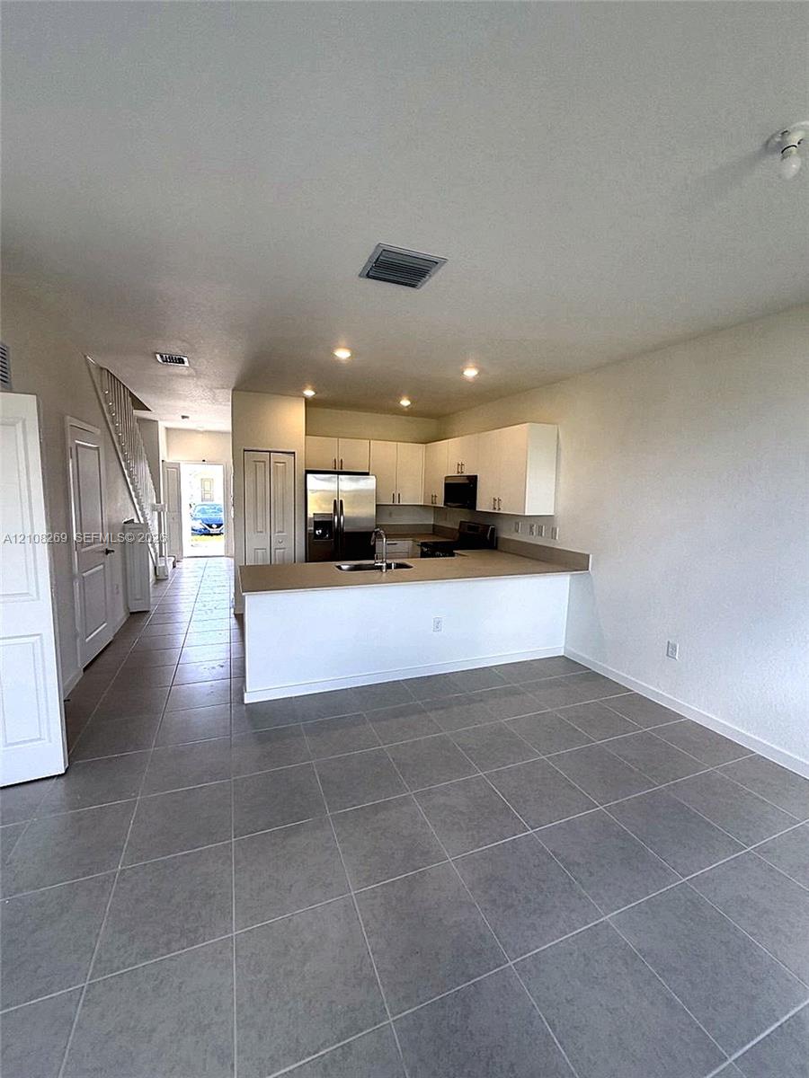 Kitchen featuring white cabinetry, solid-surface countertops, stainless steel appliances, and large-format tile flooring