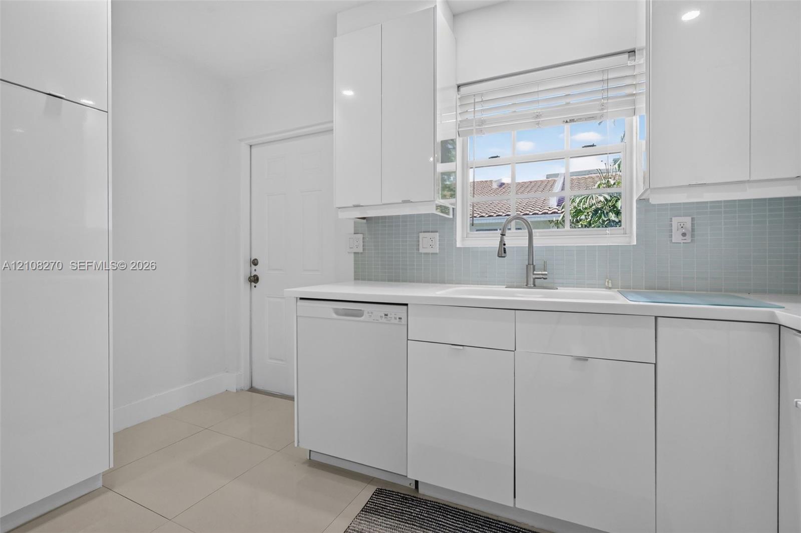 Kitchen featuring white high-gloss cabinetry, integrated dishwasher, light blue glass tile backsplash, white solid-surface countertops, and stainless steel gooseneck faucet