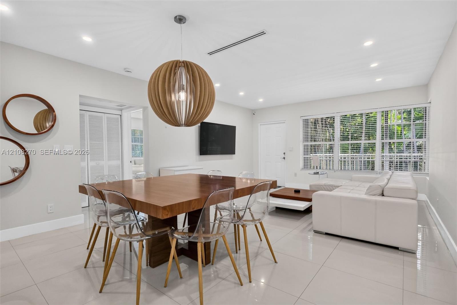 Open-concept area featuring polished tile flooring, recessed ceiling lighting, a spherical wooden pendant fixture, and large multi-pane windows