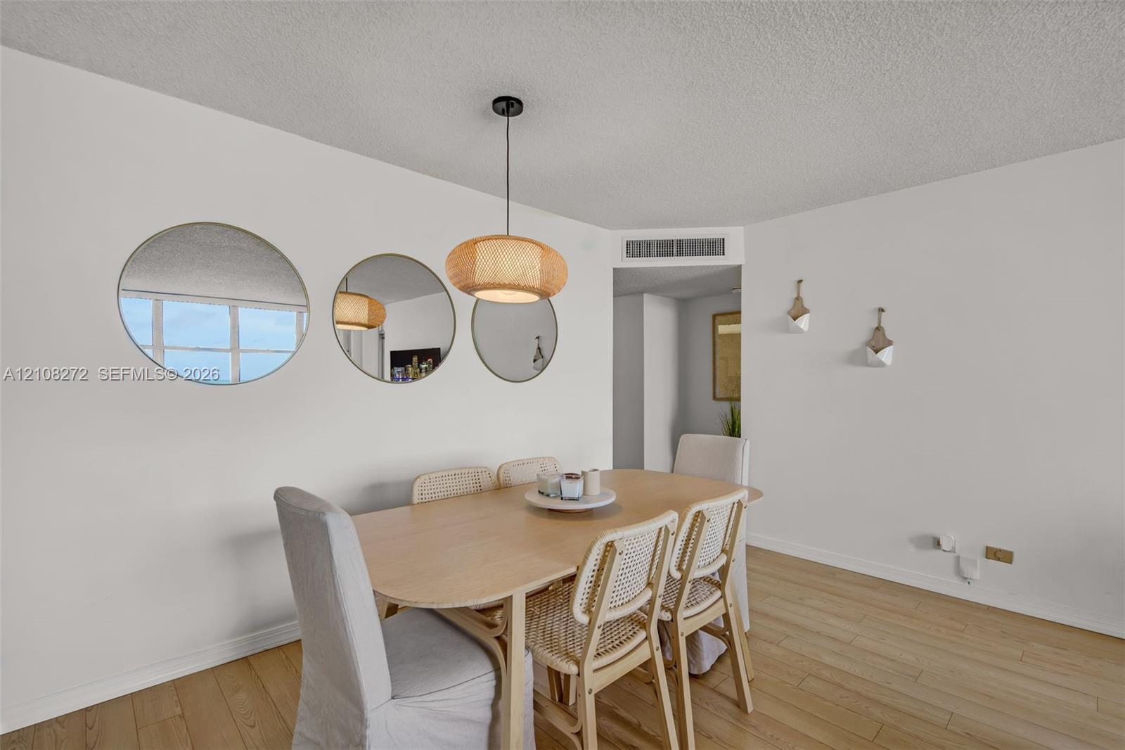 Dining area featuring wood-finish flooring, a woven pendant light fixture, three circular wall-mounted mirrors, and two built-in wall-mounted planters