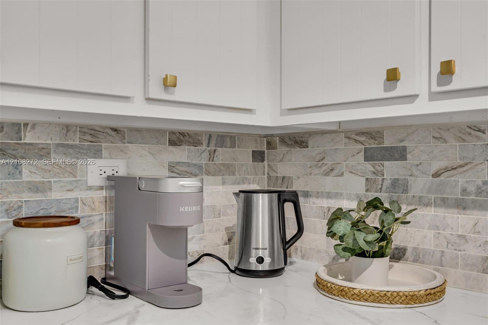 Kitchen featuring white shaker-style cabinetry, gold-tone hardware, and a natural stone tile backsplash