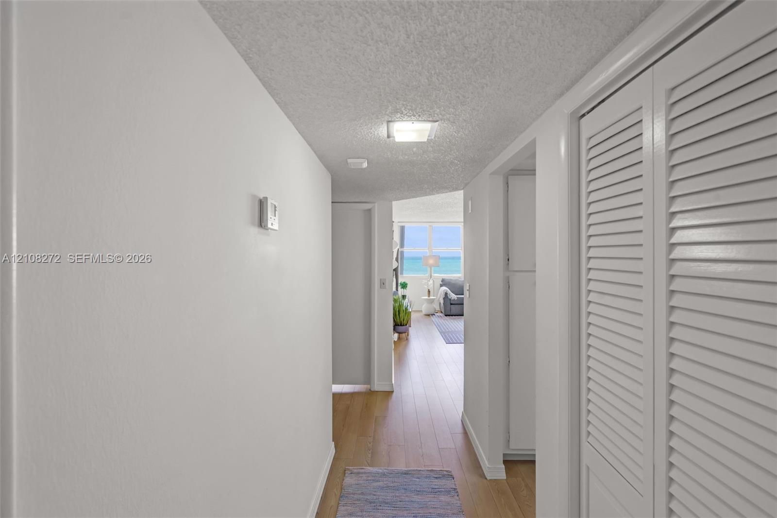 Hallway featuring wood-finish flooring, white walls, and floor-to-ceiling louvered closet doors