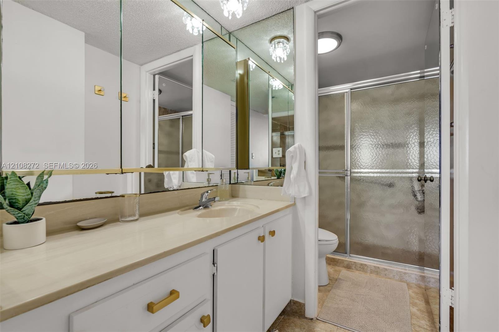 Bathroom featuring a vanity with a solid-surface countertop, integrated sink, gold-tone hardware, full-width mirror, and a walk-in shower with a sliding glass door