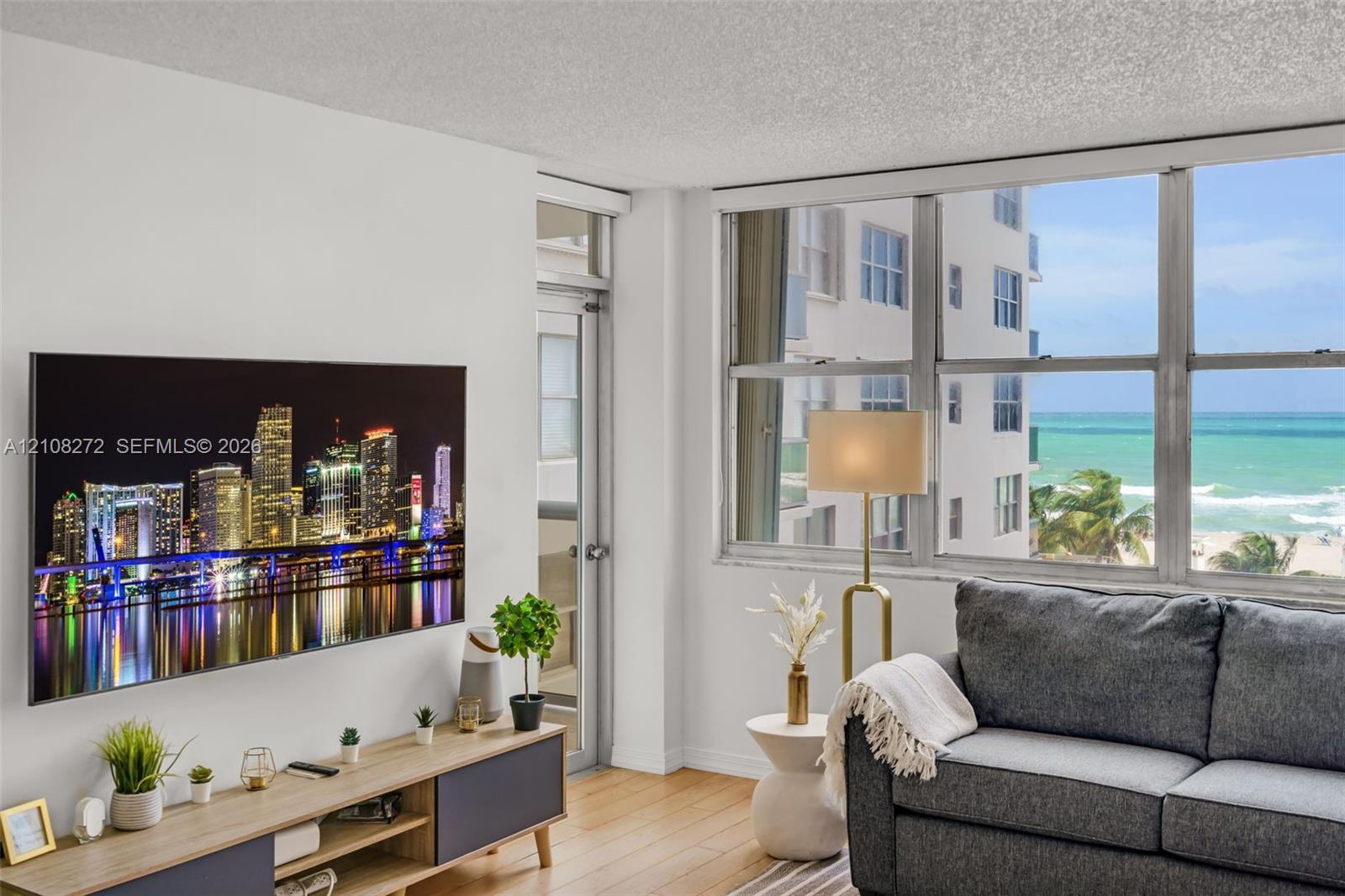Floor-to-ceiling windows featuring ocean and city skyline scenery, wood-finish flooring, and a glass-paneled exterior door