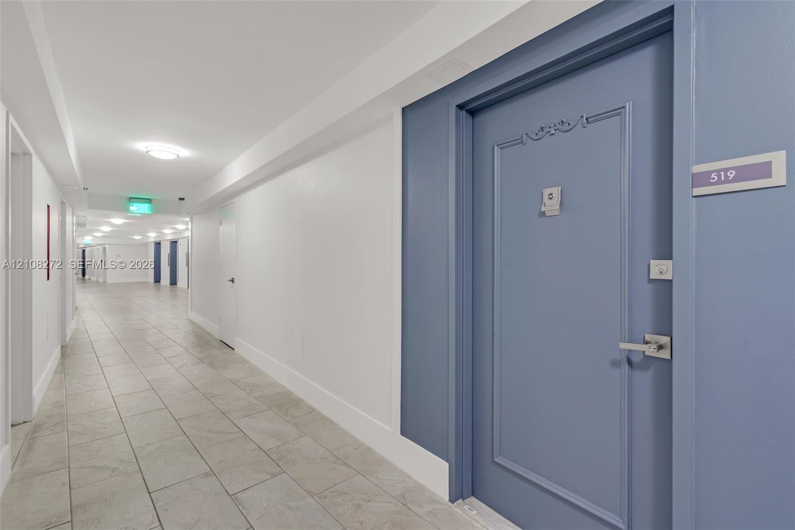 Blue paneled door with a metallic lever handle and ornate molding, polished porcelain-tile flooring, and recessed ceiling lighting
