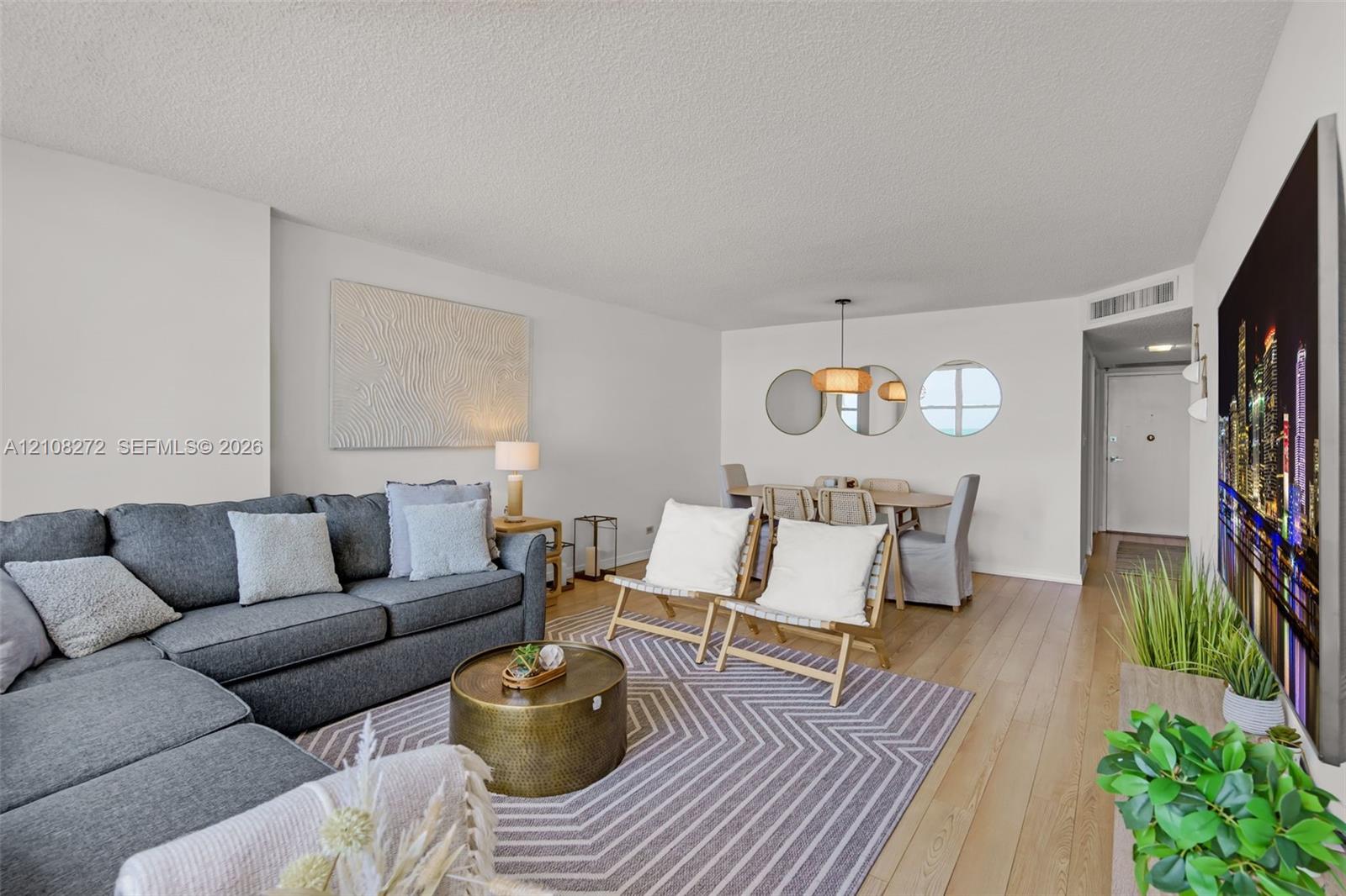 Open-concept living space featuring wood-finish flooring, textured ceiling finish, and an integrated pendant light fixture