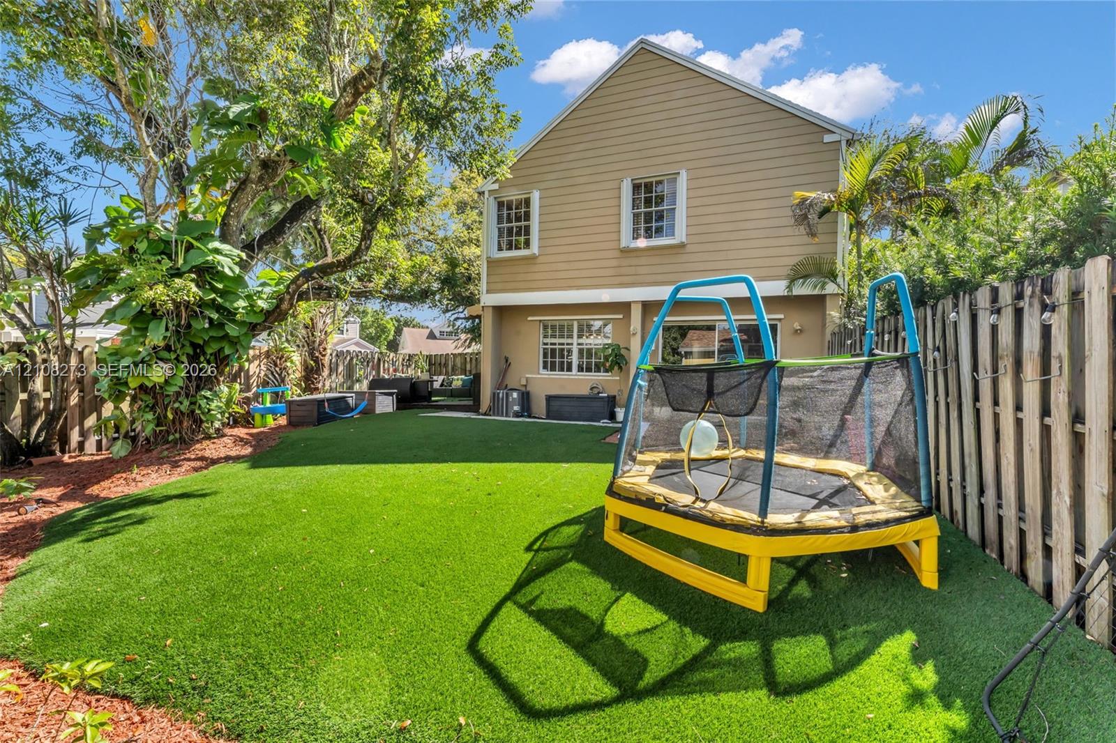 Fenced backyard featuring synthetic turf, wood-siding exterior, and mature landscaping