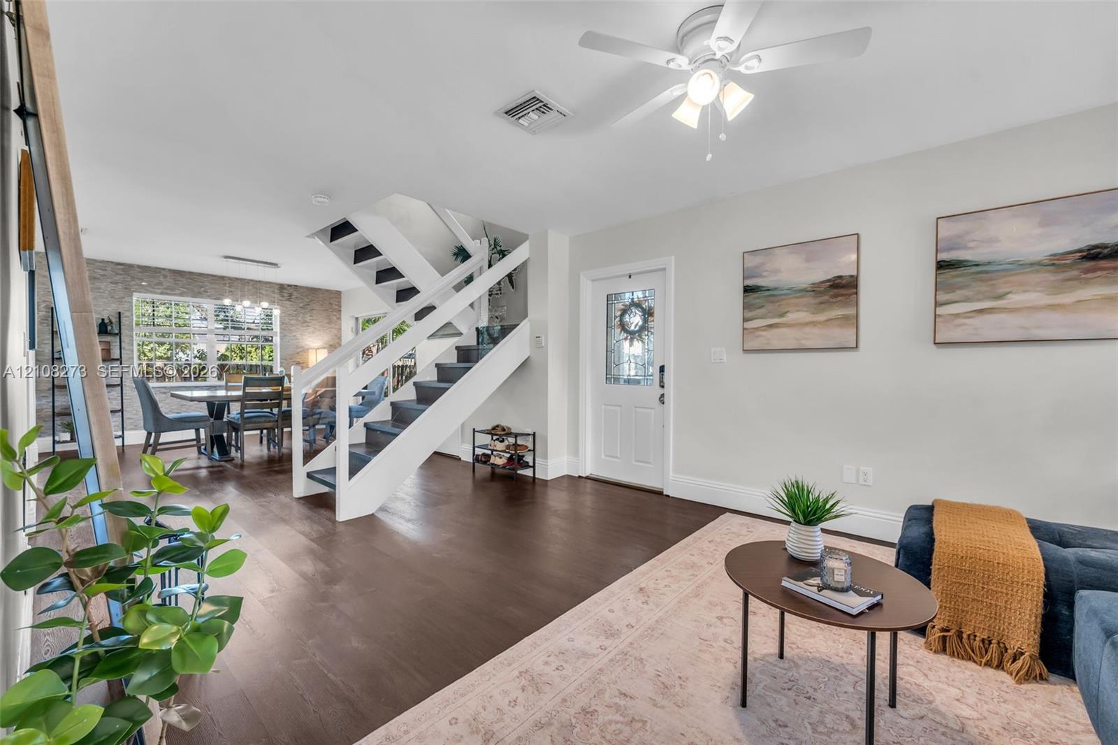 Open-concept interior featuring dark wood-finish flooring, a central staircase with white railings, textured stone-style wall detailing, and a glass-paneled entry door