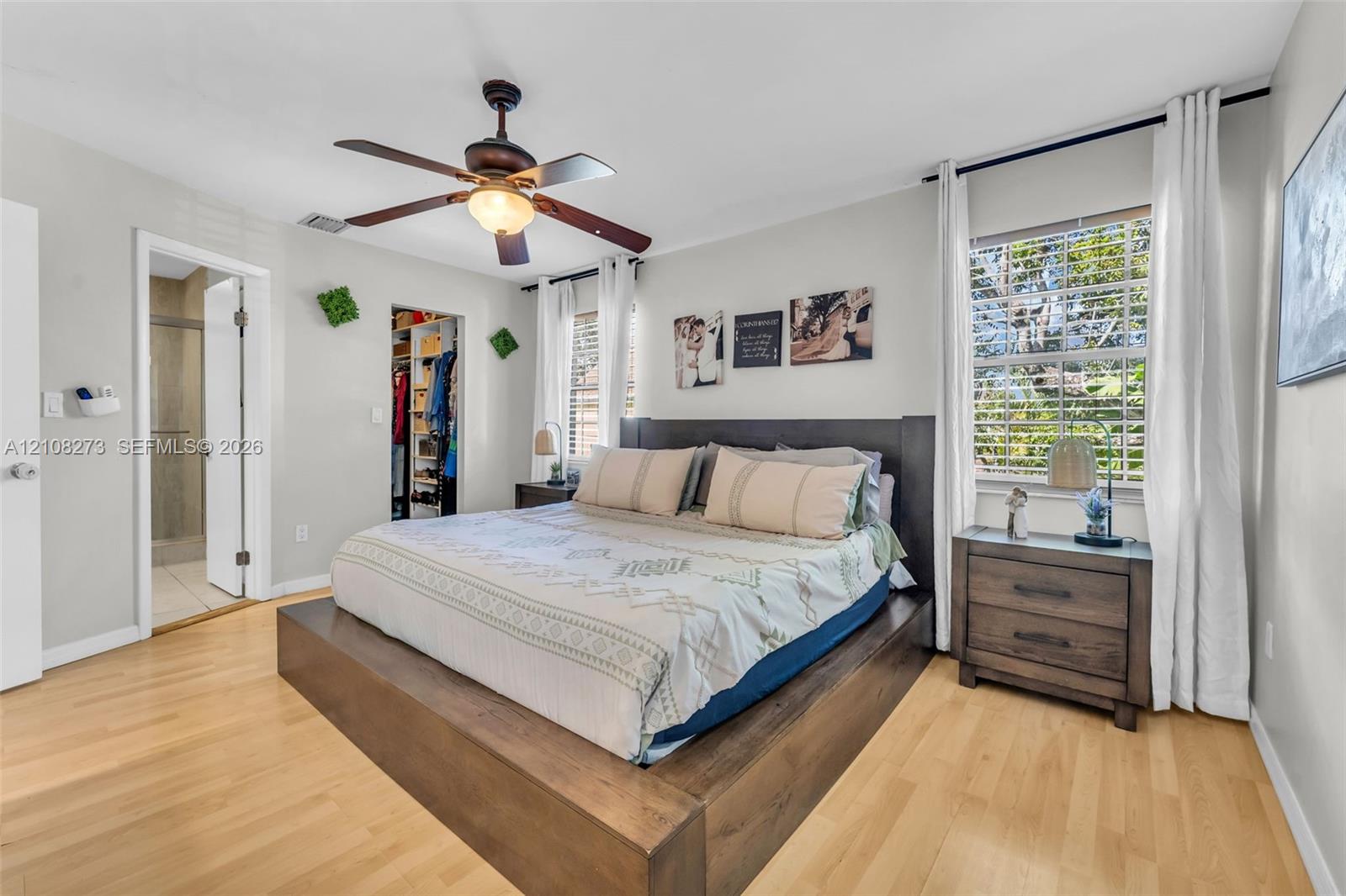 Bedroom featuring light wood-finish flooring, a ceiling fan with integrated lighting, and a walk-in closet with built-in organization