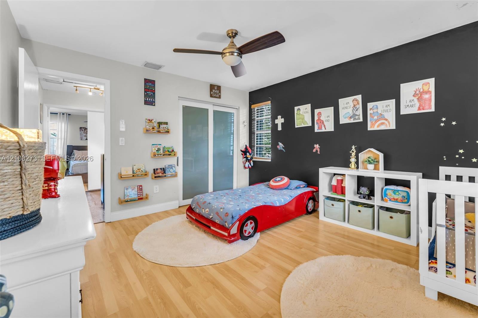 Wood-finish flooring, brushed metal ceiling fan with integrated light fixture, contrast accent wall, and sliding glass closet doors