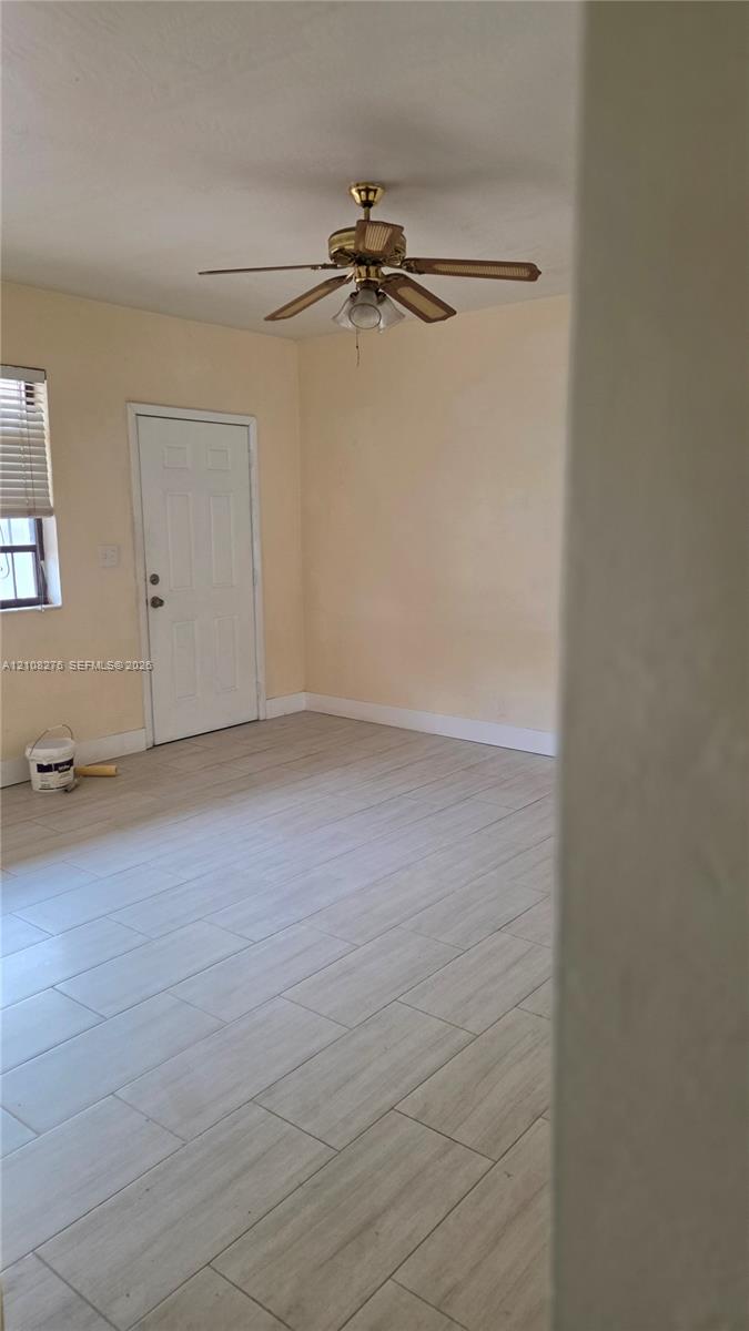 Interior space featuring light-toned tile flooring, a multi-blade ceiling fan, and a single-pane window with horizontal blinds