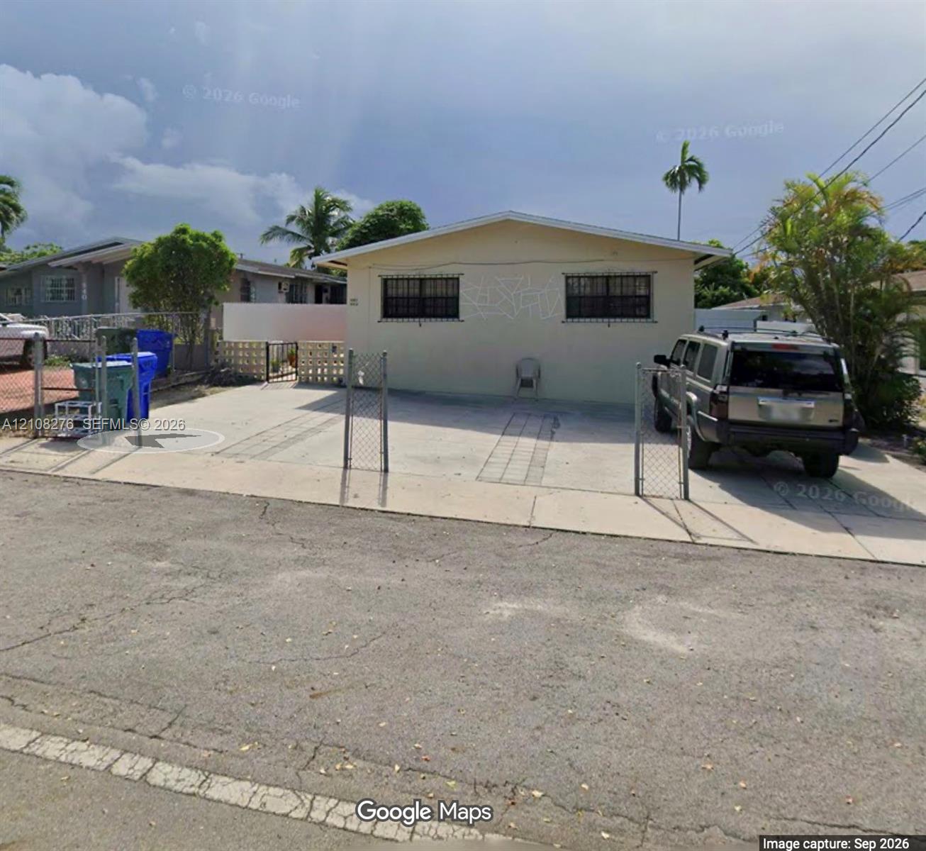 Single-story residence featuring a concrete driveway, metal chain-link perimeter fencing, and exterior window security bars