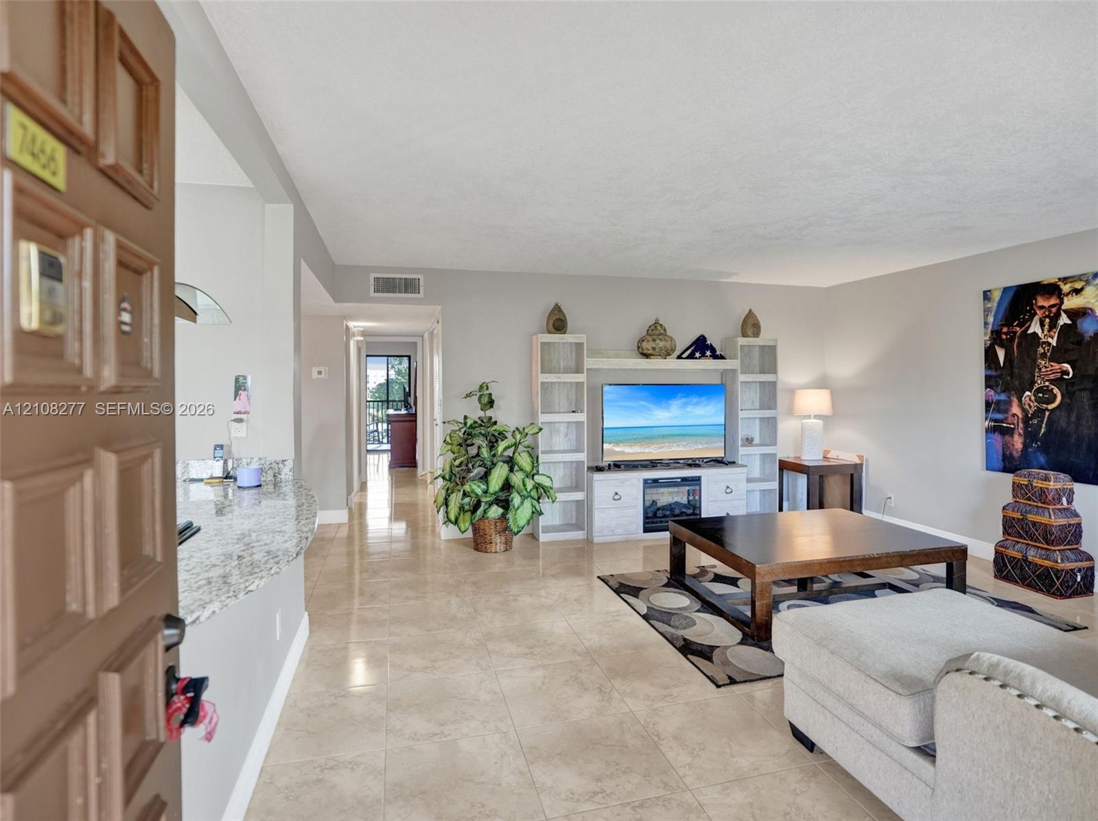 Open-concept interior featuring neutral stone-finish tile flooring, a stone-surfaced breakfast bar, and a built-in media center with integrated fireplace