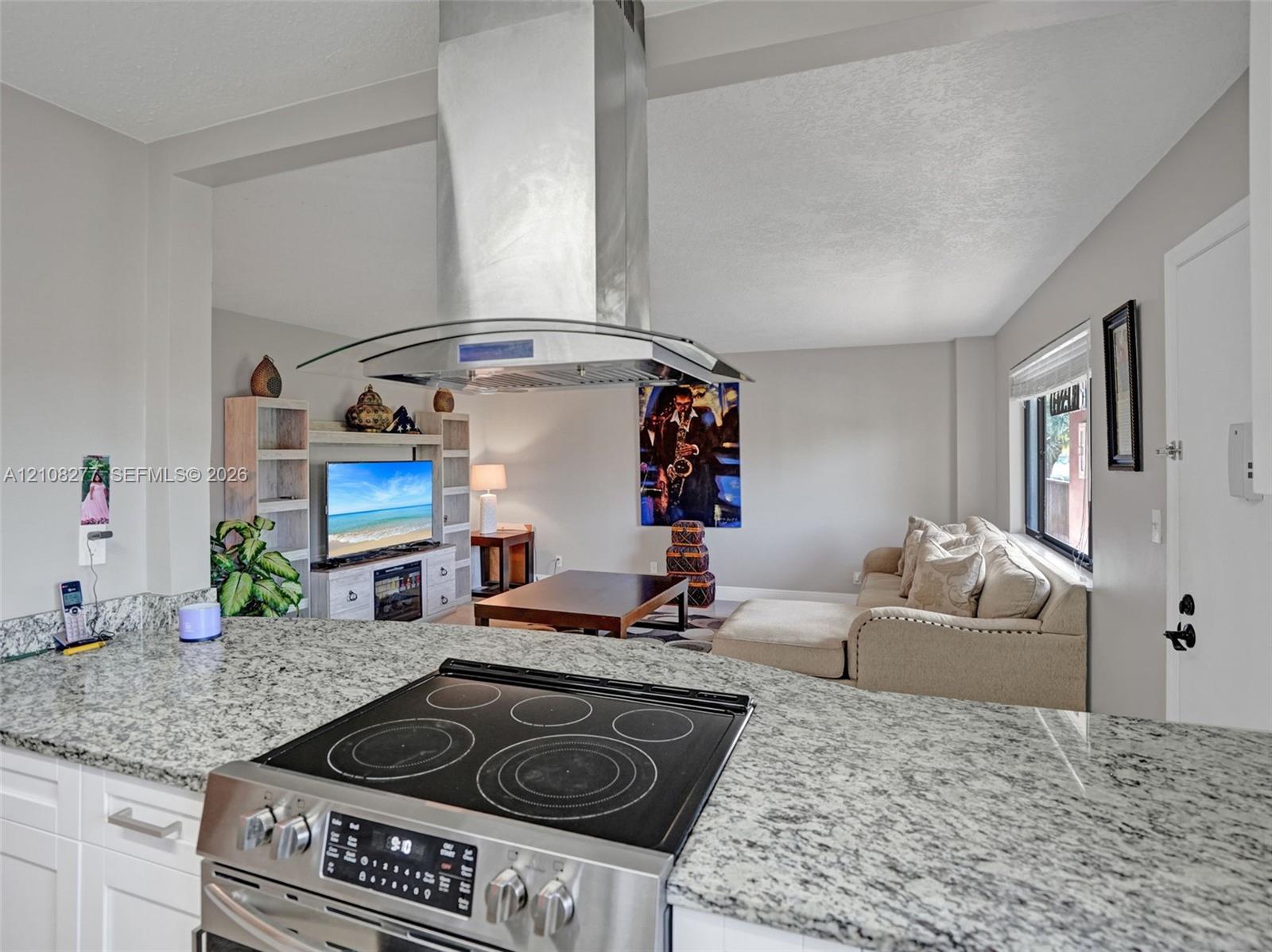 Kitchen featuring stone-finish countertops, stainless steel electric range, island-mounted stainless steel chimney hood, and built-in white cabinetry