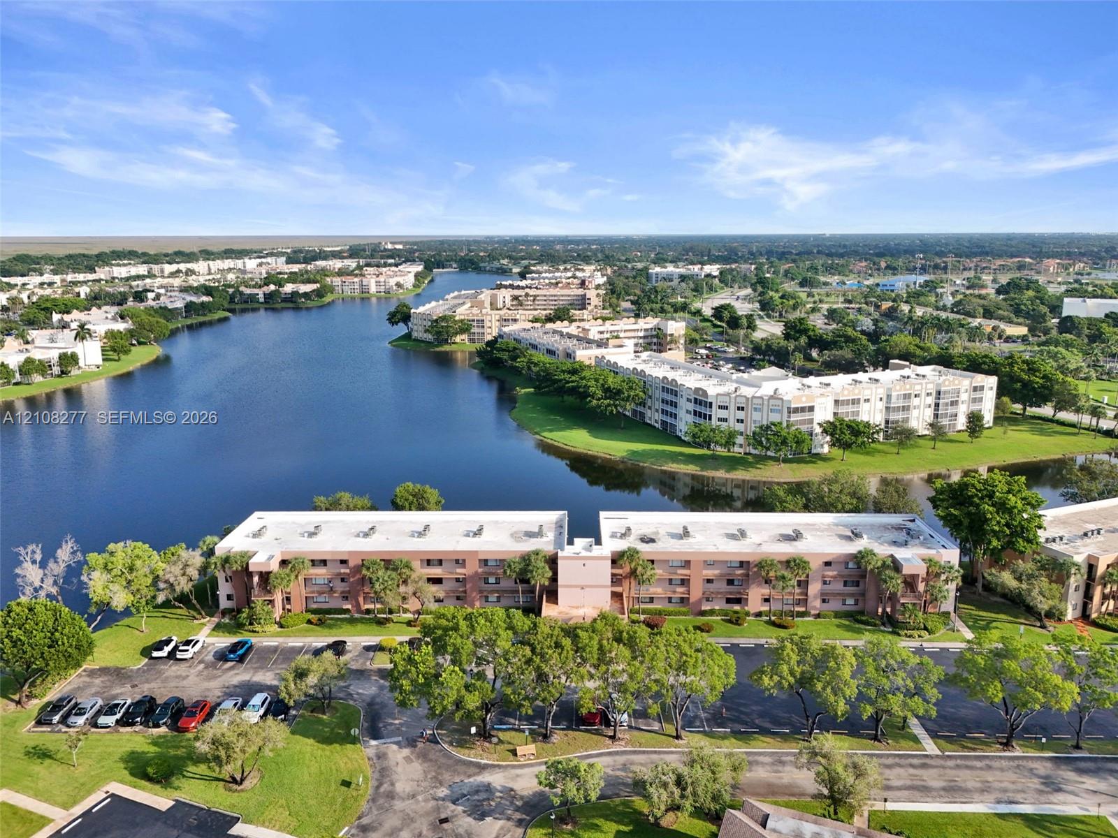 Aerial perspective of a multi-story residential building featuring exterior masonry cladding, paved parking areas, and mature landscaping situated on a waterfront lot
