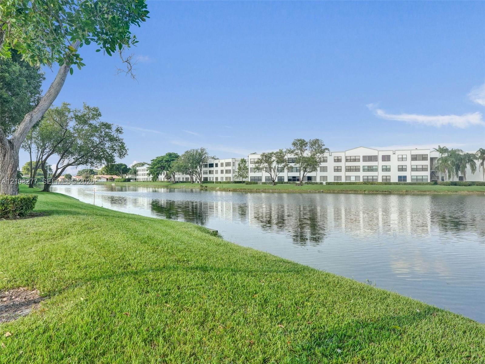 Waterfront property featuring a manicured lawn, mature trees, and a lake shoreline