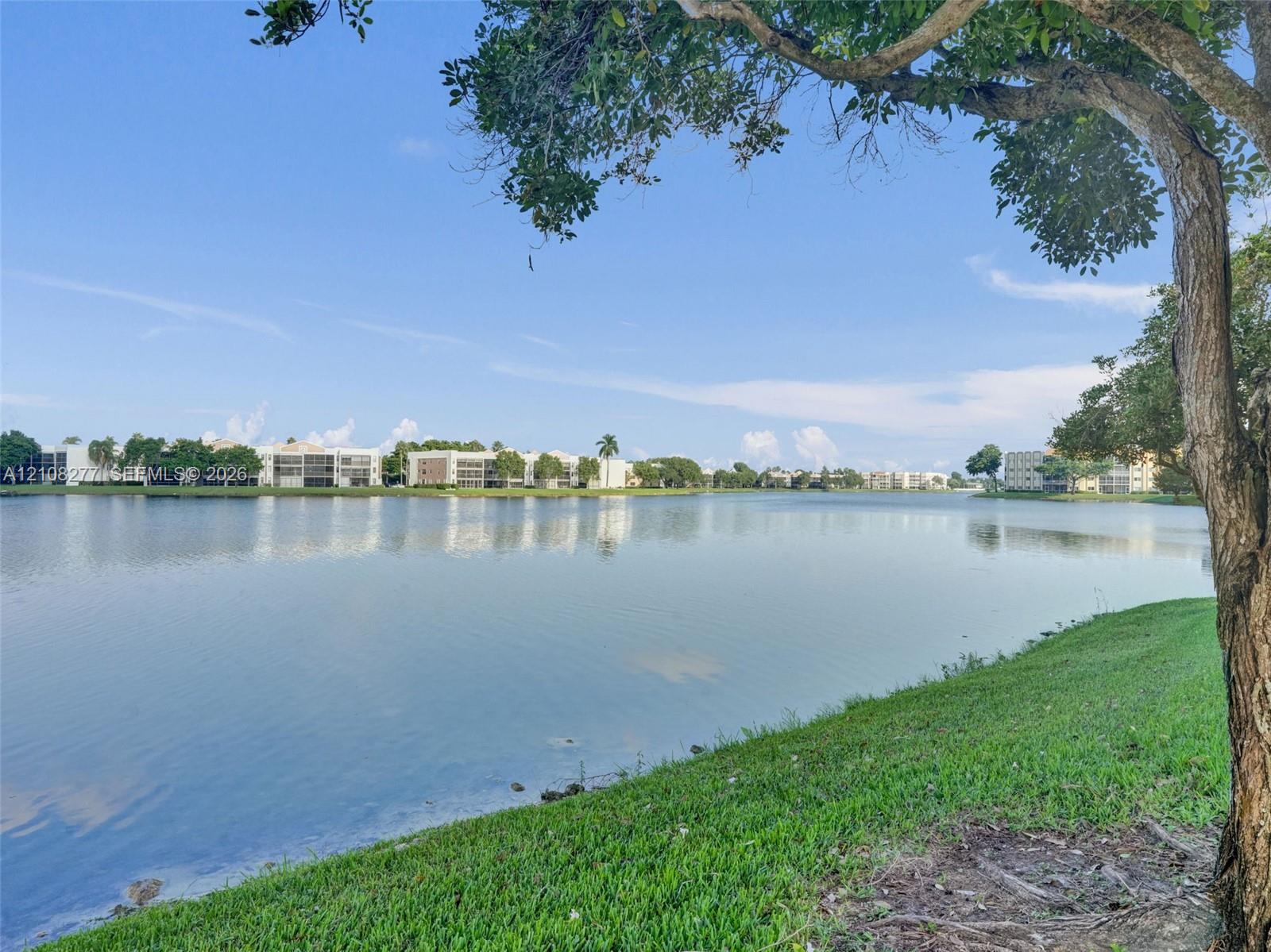 Waterfront scenery featuring a expansive lake, manicured grass shoreline, and mature trees