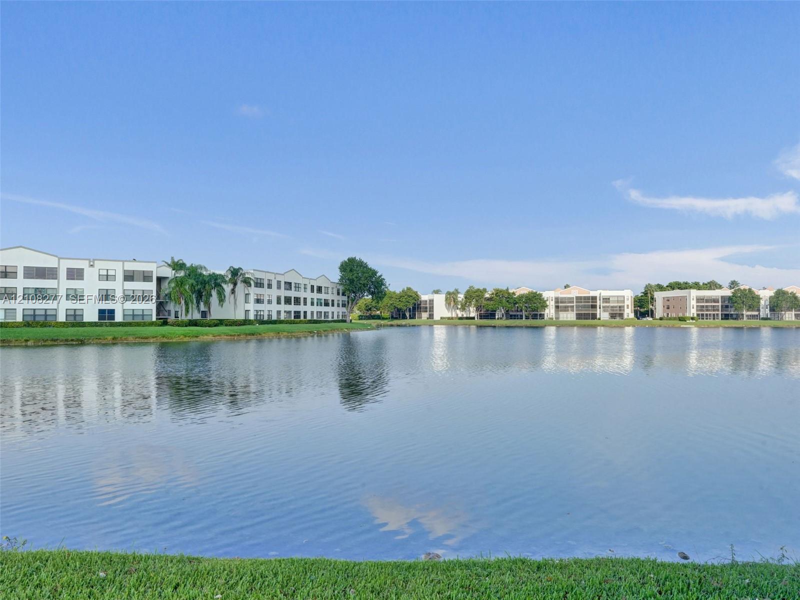 Waterfront setting featuring a multi-story exterior with stucco finish and a manicured grass perimeter