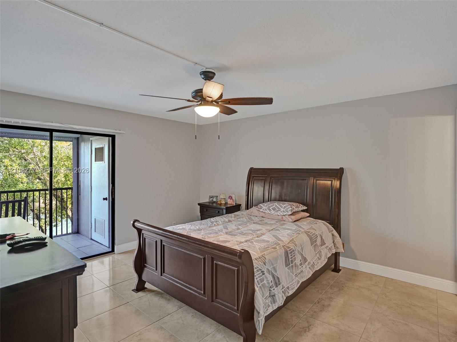 Large-format tile flooring, ceiling fan with integrated lighting, and a sliding glass door providing access to a private balcony