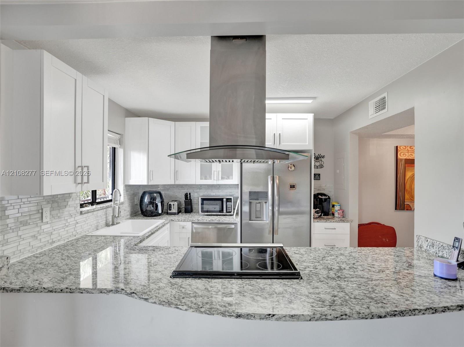 Kitchen featuring stone-finish countertops, stainless steel chimney-style range hood, electric cooktop, white cabinetry, and a subway tile backsplash