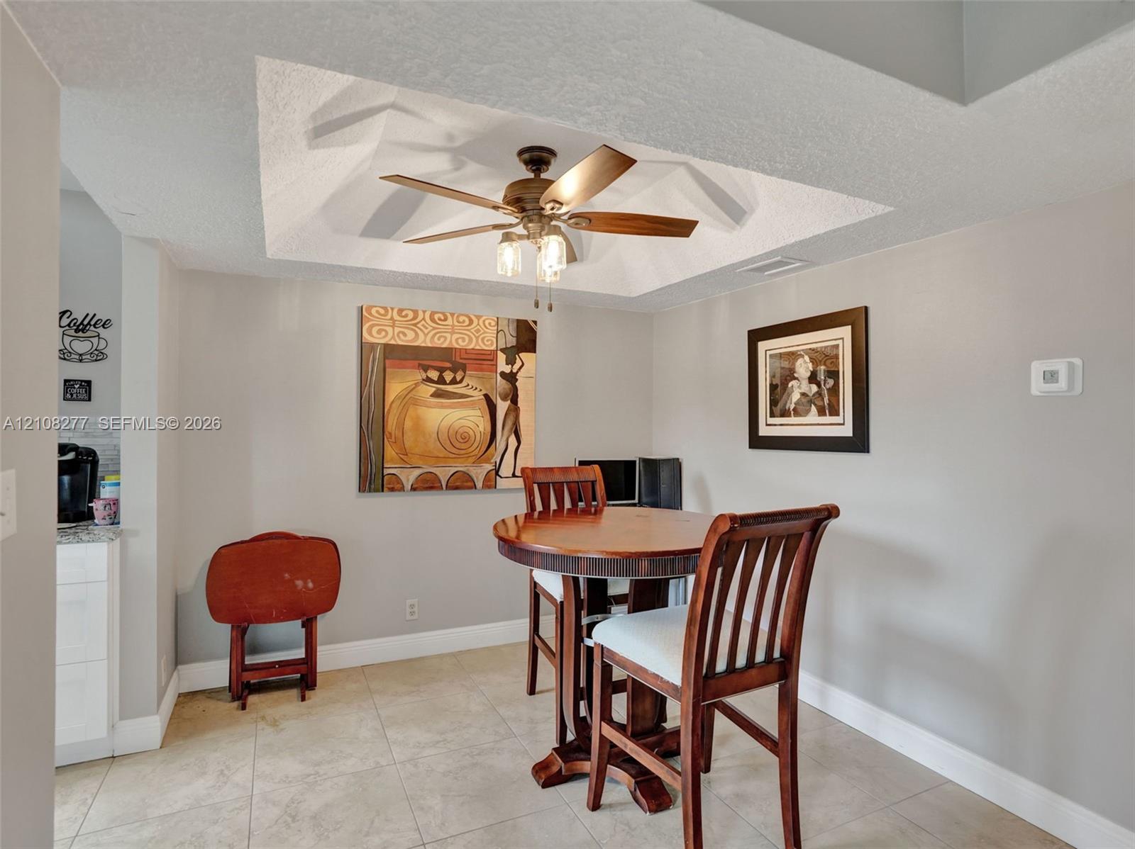 Tray ceiling featuring a central five-blade ceiling fan with integrated lighting and neutral ceramic tile flooring