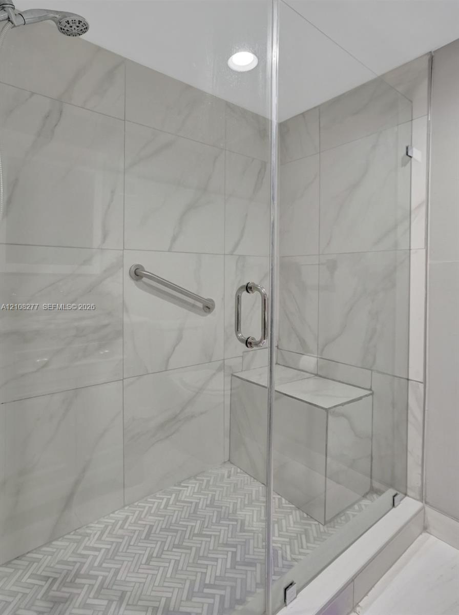 Walk-in shower featuring large-format porcelain wall tile, herringbone-patterned floor tile, frameless glass enclosure, built-in tile bench, and polished chrome hardware