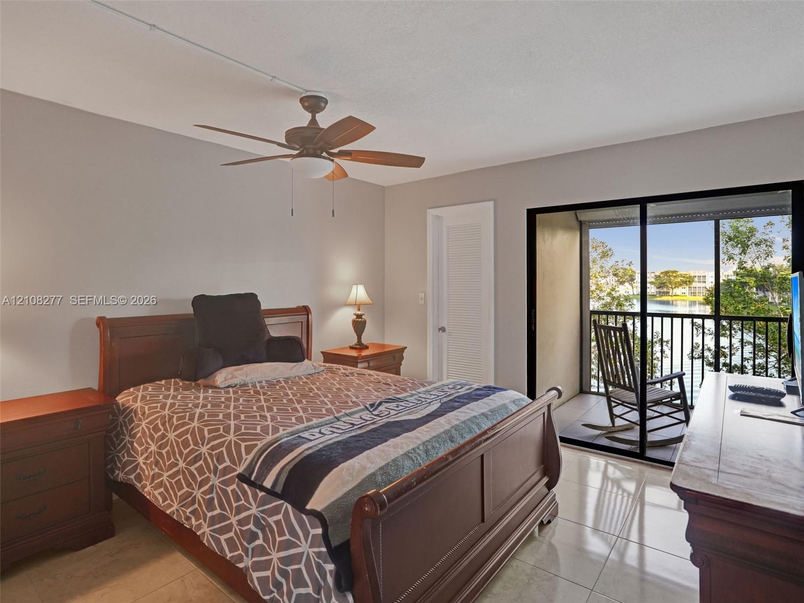 Spacious room featuring polished tile flooring, a multi-blade ceiling fan, and sliding glass doors opening to a private balcony with water scenery