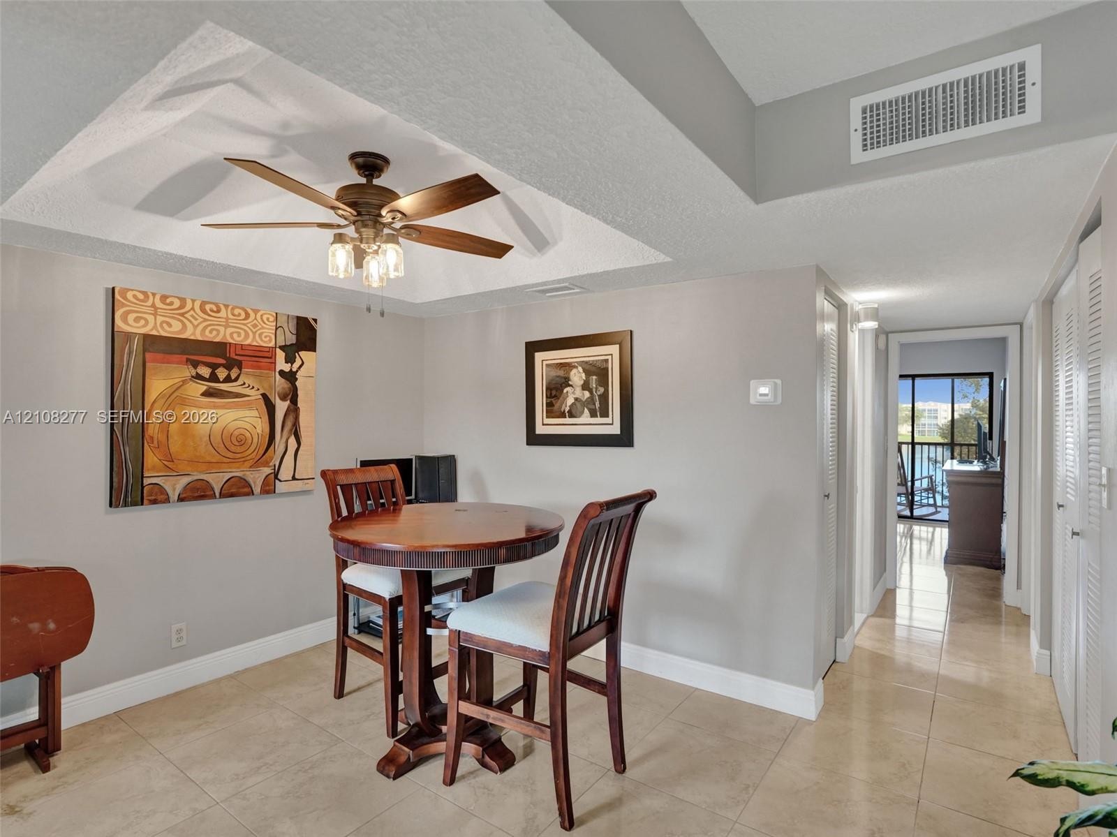 Tray ceiling featuring a central five-blade ceiling fan with integrated light fixture, neutral wall finishes, and large-format tile flooring