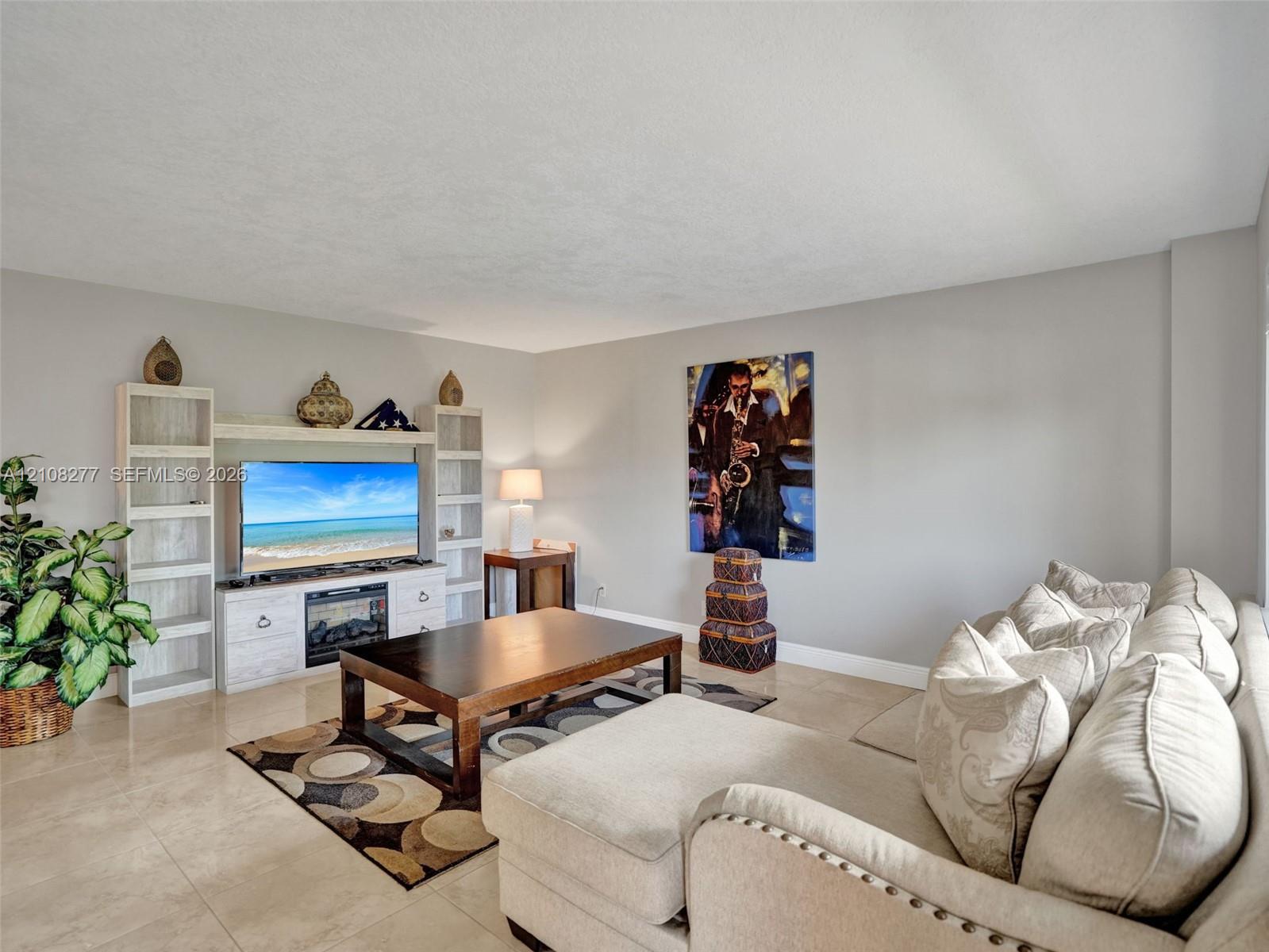 Living area featuring light-toned tile flooring, neutral wall paint, and built-in cabinetry surrounding an integrated electric fireplace