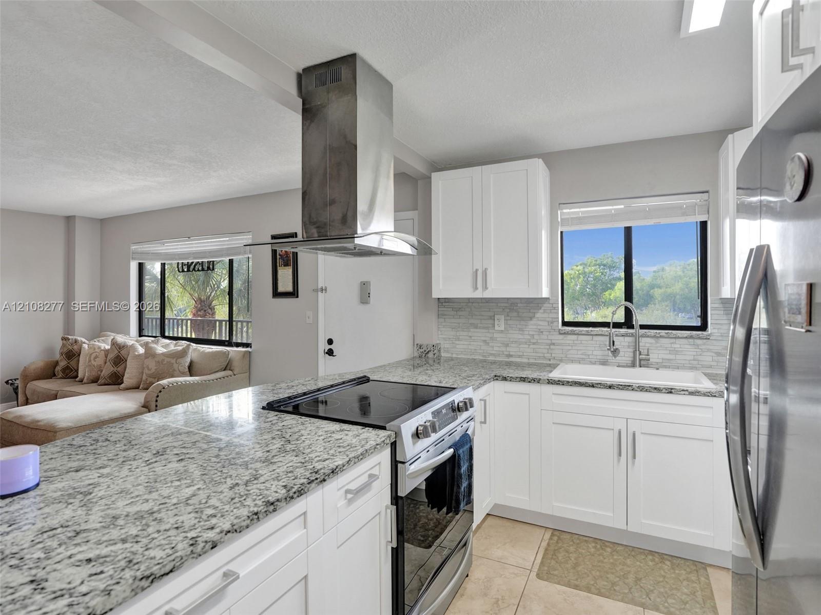 Kitchen featuring white shaker-style cabinetry, stone countertops, stainless steel range with a wall-mounted chimney hood, tiled backsplash, and an undermount sink