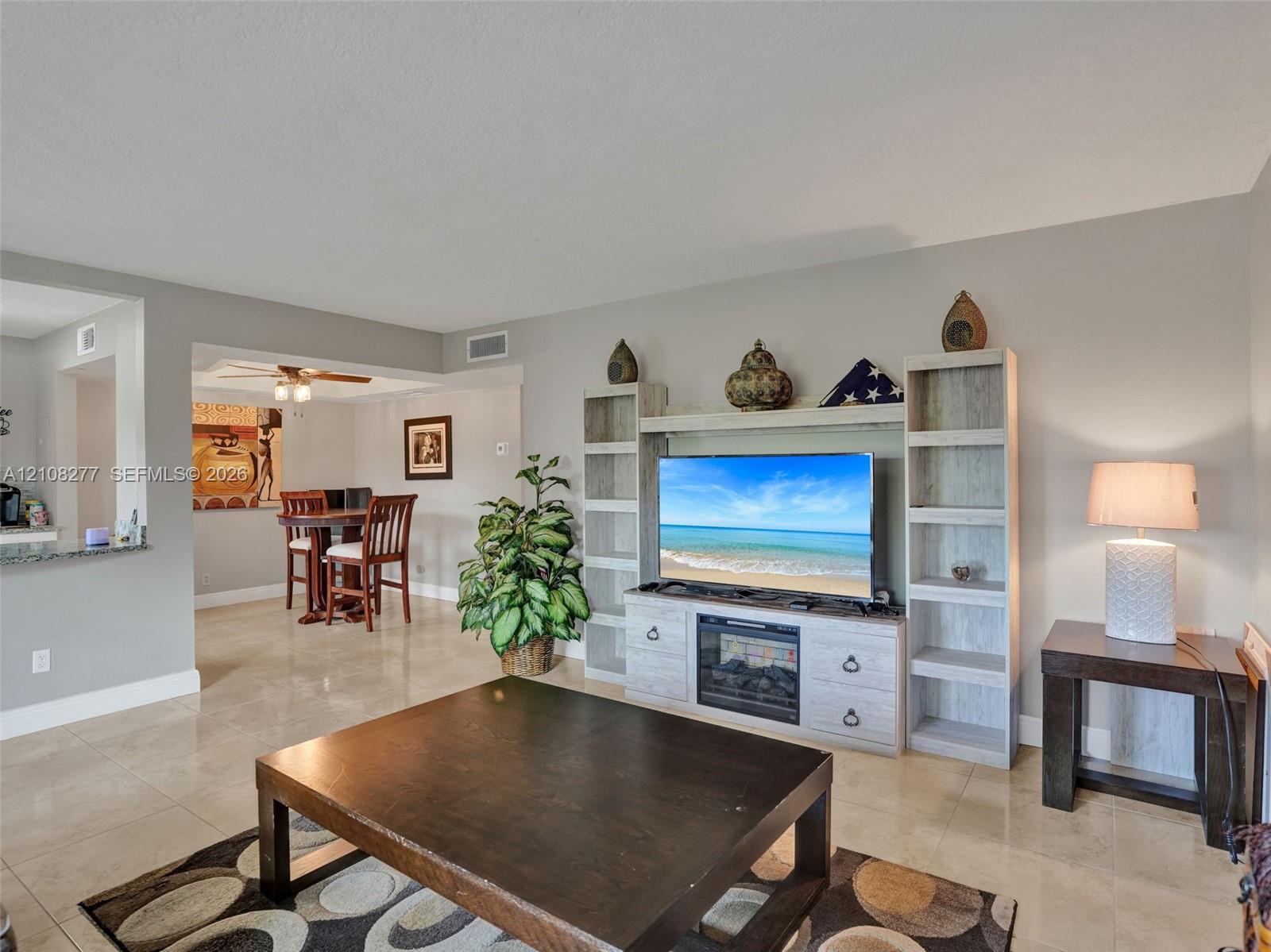 Neutral-toned tile flooring throughout an open living area featuring a custom built-in entertainment center with integrated shelving and an electric fireplace insert