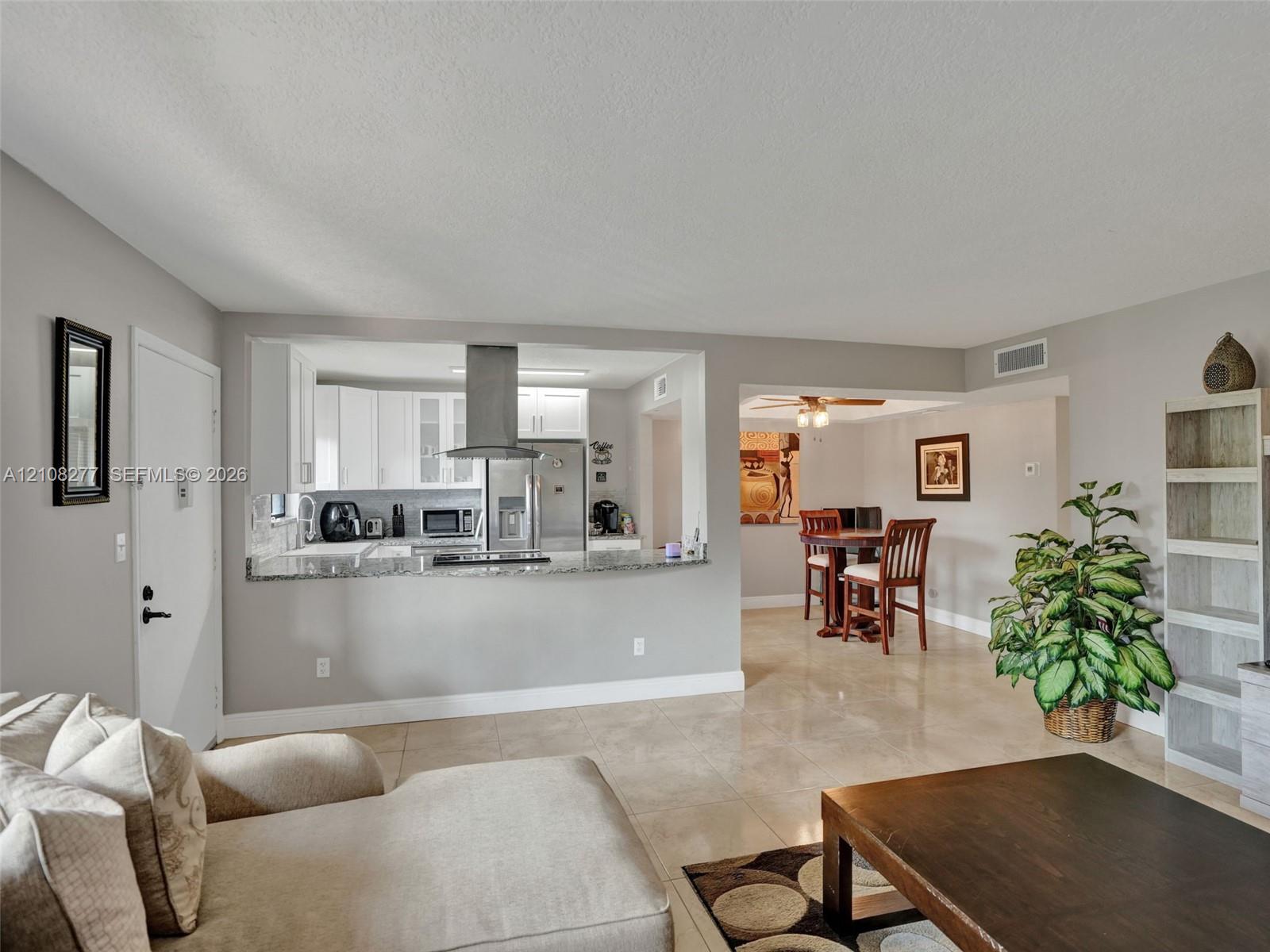 Kitchen featuring white cabinetry, stone-finish countertops, and a stainless steel range hood, complemented by large-format tile flooring throughout
