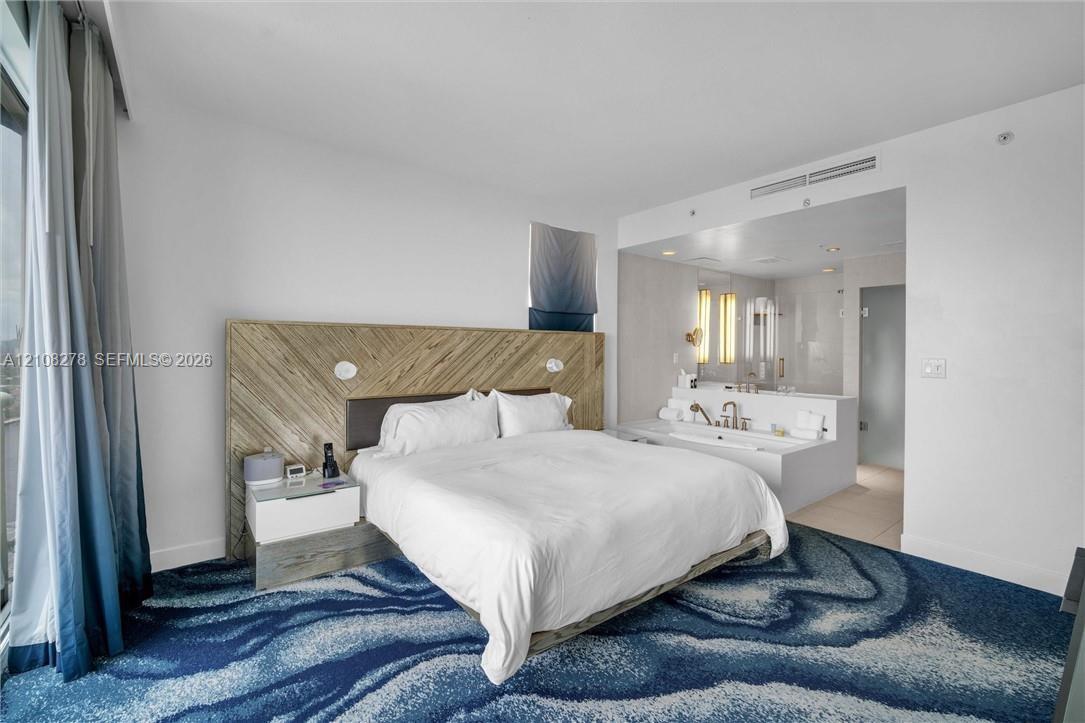 Wood-finish slat accent wall, built-in bedside cabinetry, recessed ceiling lighting, and a soaking tub with integrated vanity