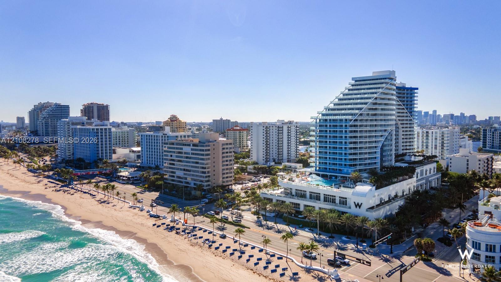 Aerial perspective of a high-rise building featuring glass-balcony facades, an elevated podium pool, and a location positioned directly along the beachfront