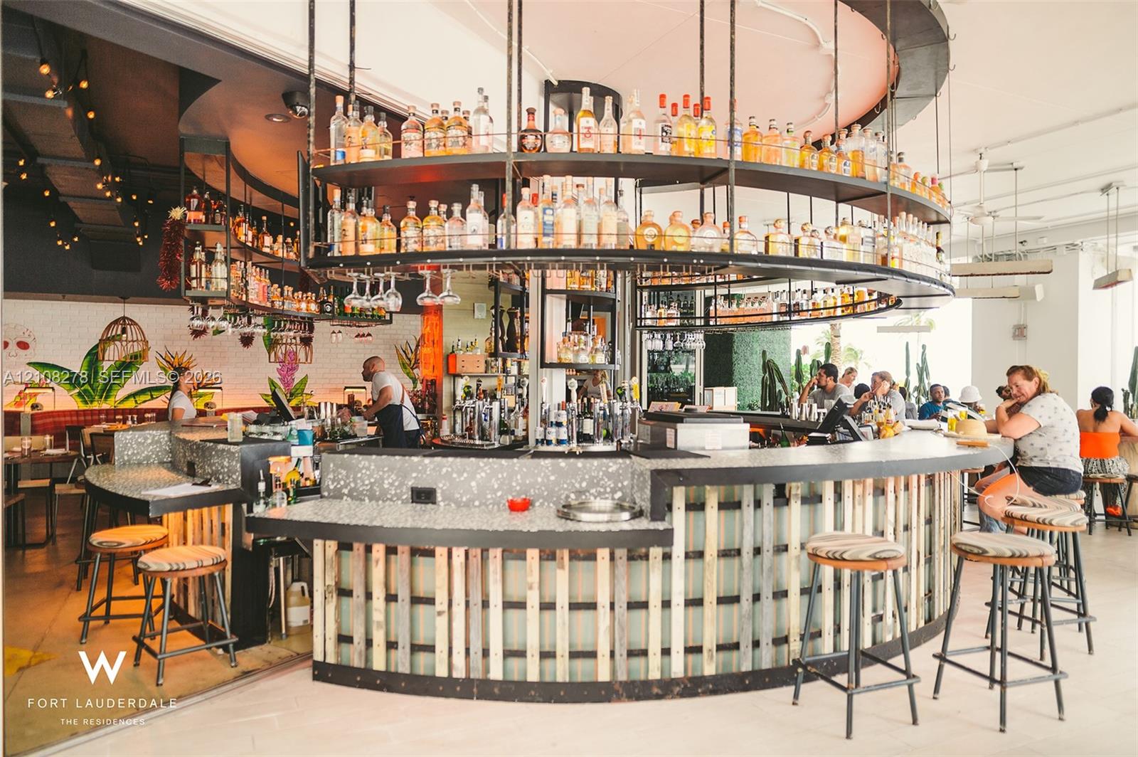 Circular bar featuring a speckled composite countertop, vertical wood-slat paneling, and an overhead tiered metal shelving system