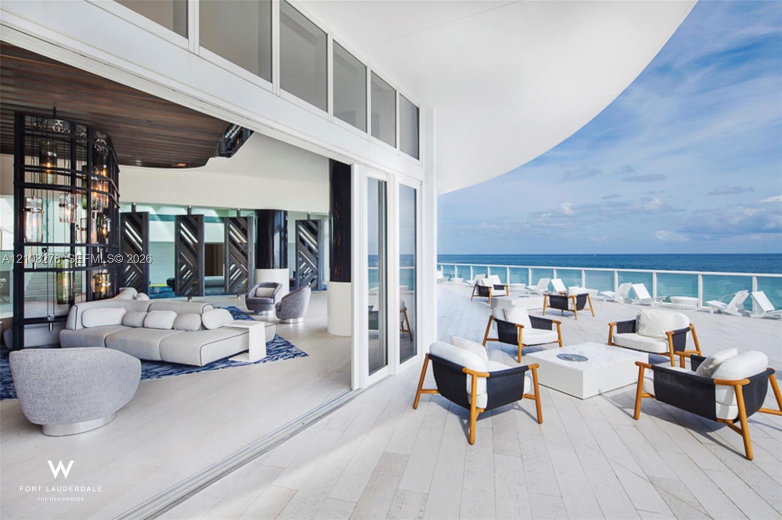 Expansive covered balcony featuring white tile flooring, glass perimeter railing, and large multi-panel sliding glass doors