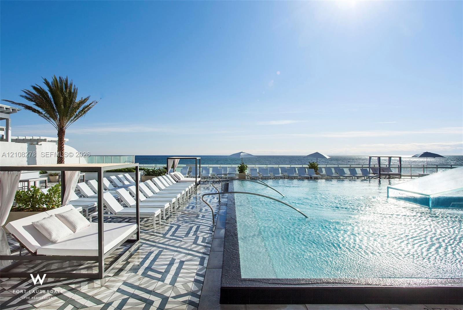 Infinity-edge swimming pool featuring a patterned tile deck, metal-framed structures, and a glass-paneled perimeter railing