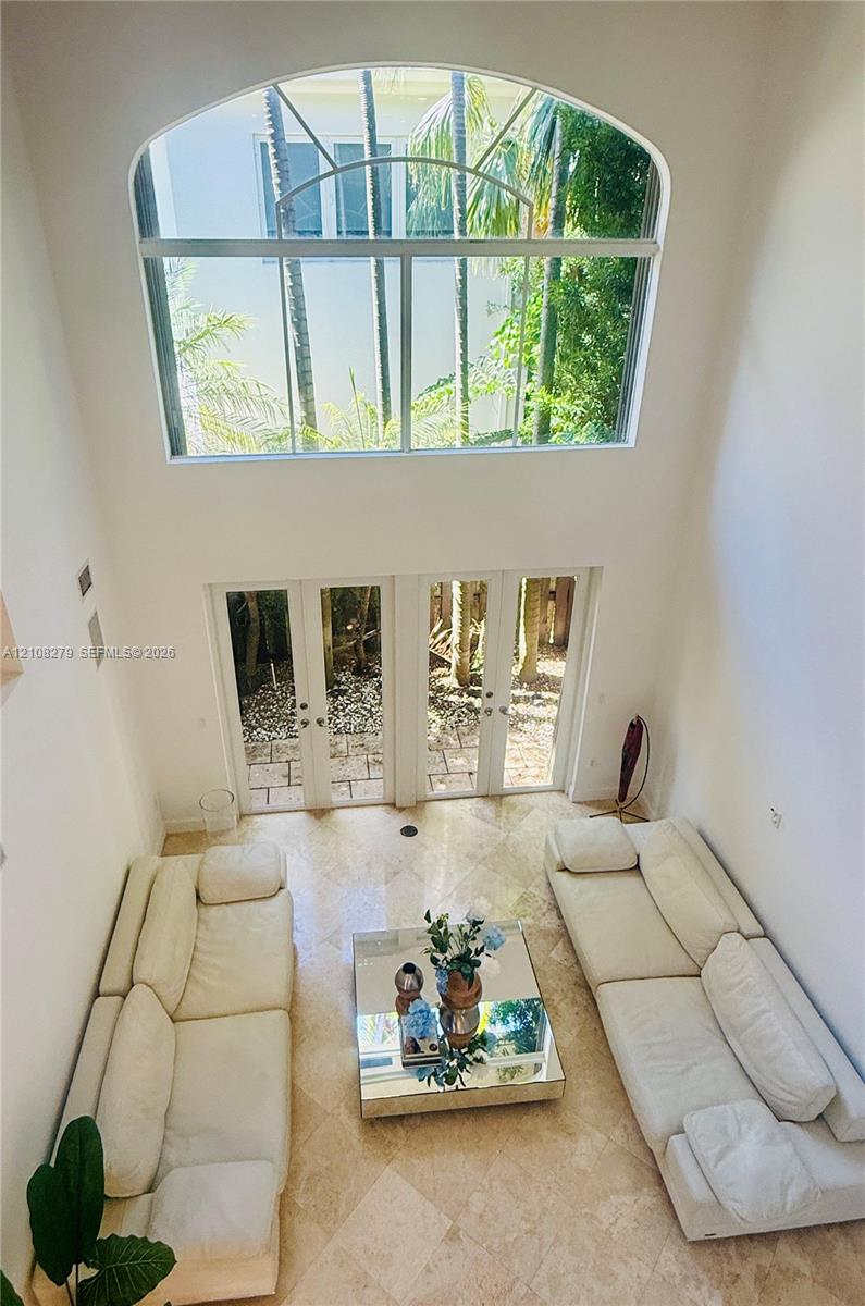 Double-height room featuring vaulted ceilings, a large arched window, and dual glass-paned doors with stone tile flooring