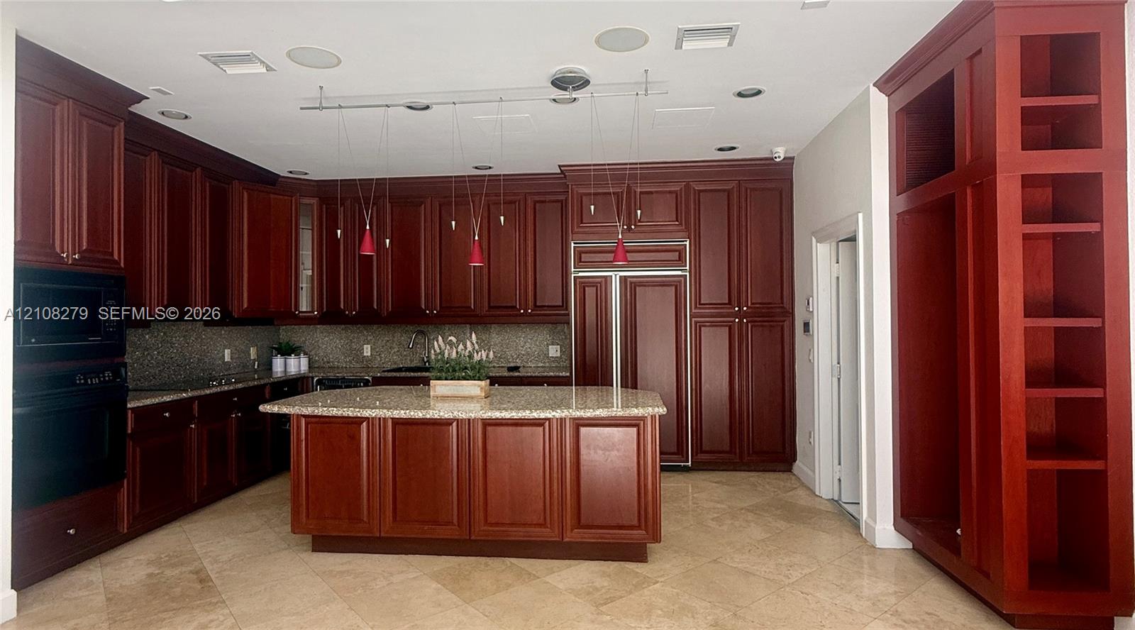 Kitchen featuring deep-toned custom cabinetry, central island with stone countertop, built-in panel-ready refrigerator, integrated wall oven, and stone tile flooring