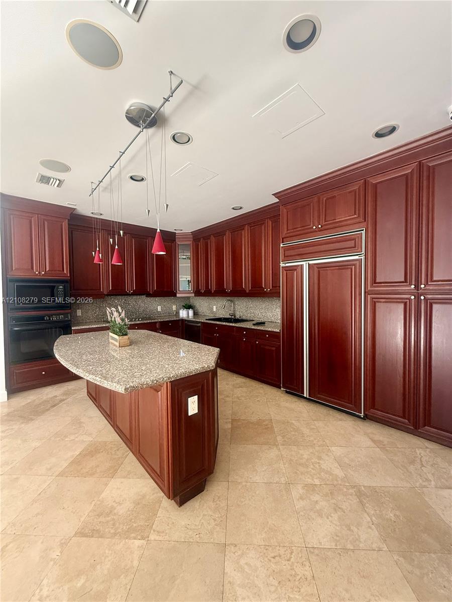 Kitchen featuring stained cabinetry, stone countertops, central island, integrated refrigerator, and recessed ceiling lighting