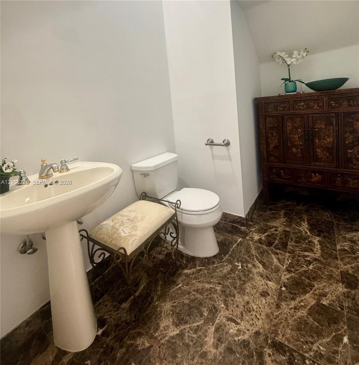 Pedestal sink with metallic faucet, white toilet, and polished stone flooring