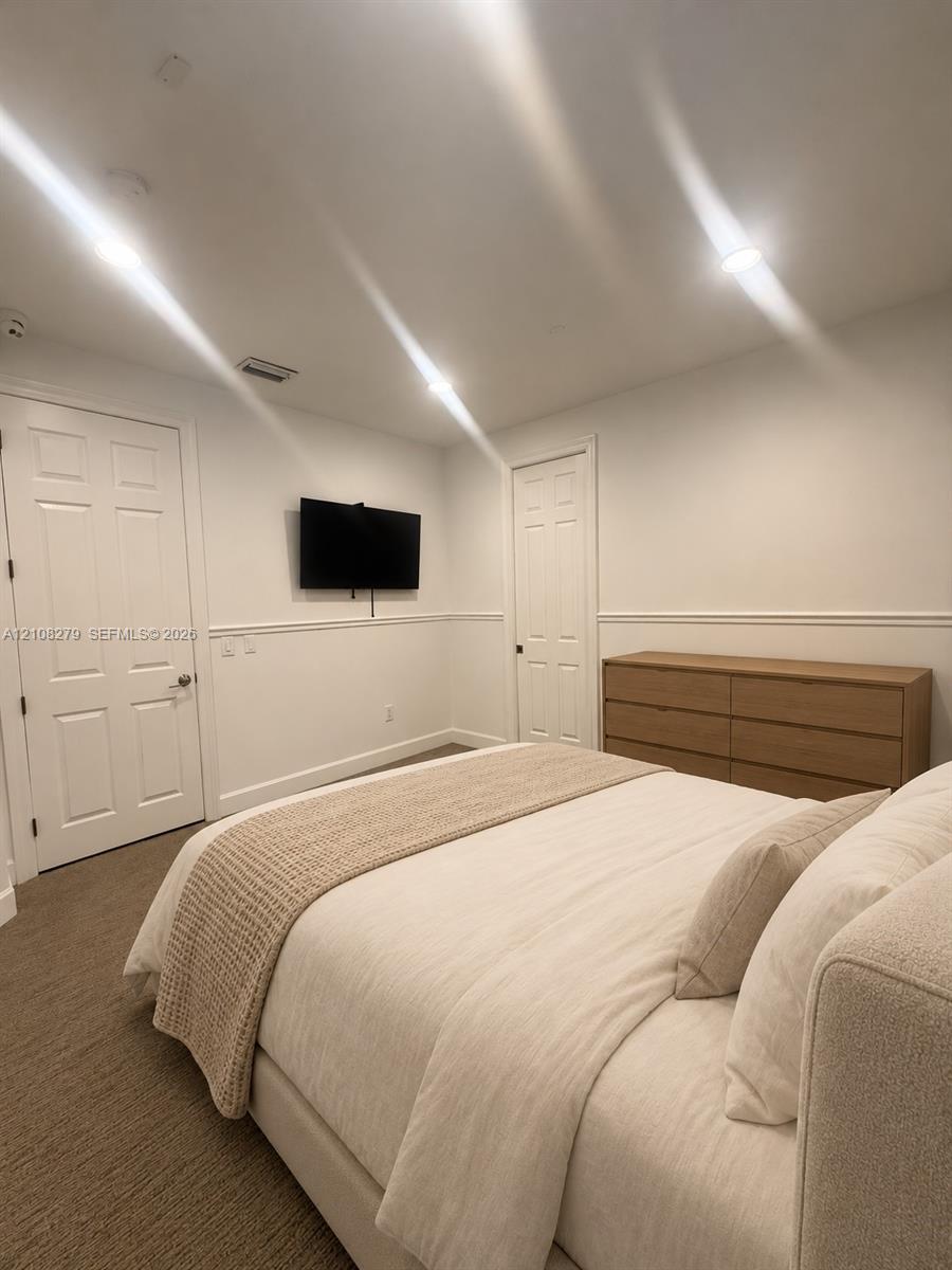 Neutral-toned carpeted flooring, wall-mounted television, recessed lighting, chair rail molding, and two-panel interior doors