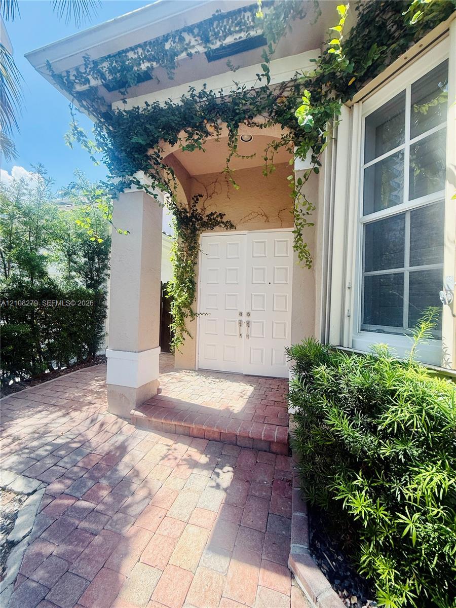 Covered entryway featuring a brick paver walkway, double doors with paneled detailing, a neutral-toned exterior, and integrated structural columns