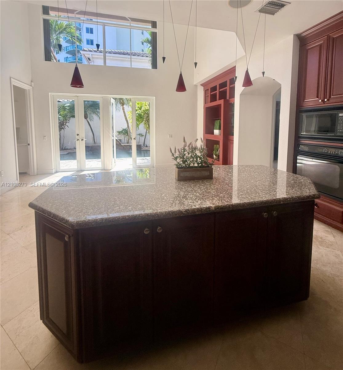 Kitchen island with a stone countertop and dark wood-finish cabinetry, vaulted ceilings, multi-light pendant fixture, double wall oven, and French doors featuring transom windows