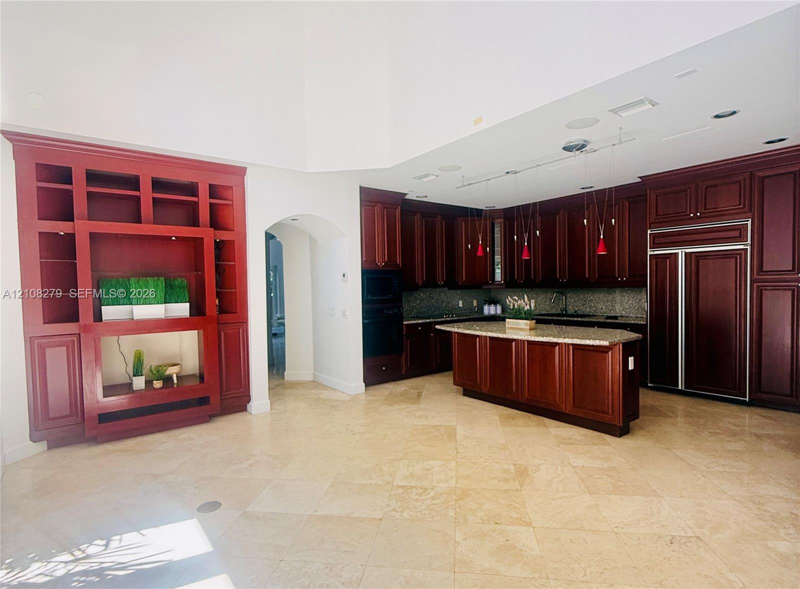 Kitchen featuring custom stained-wood cabinetry, stone countertops, central island, built-in panel-ready refrigerator, and stone tile flooring
