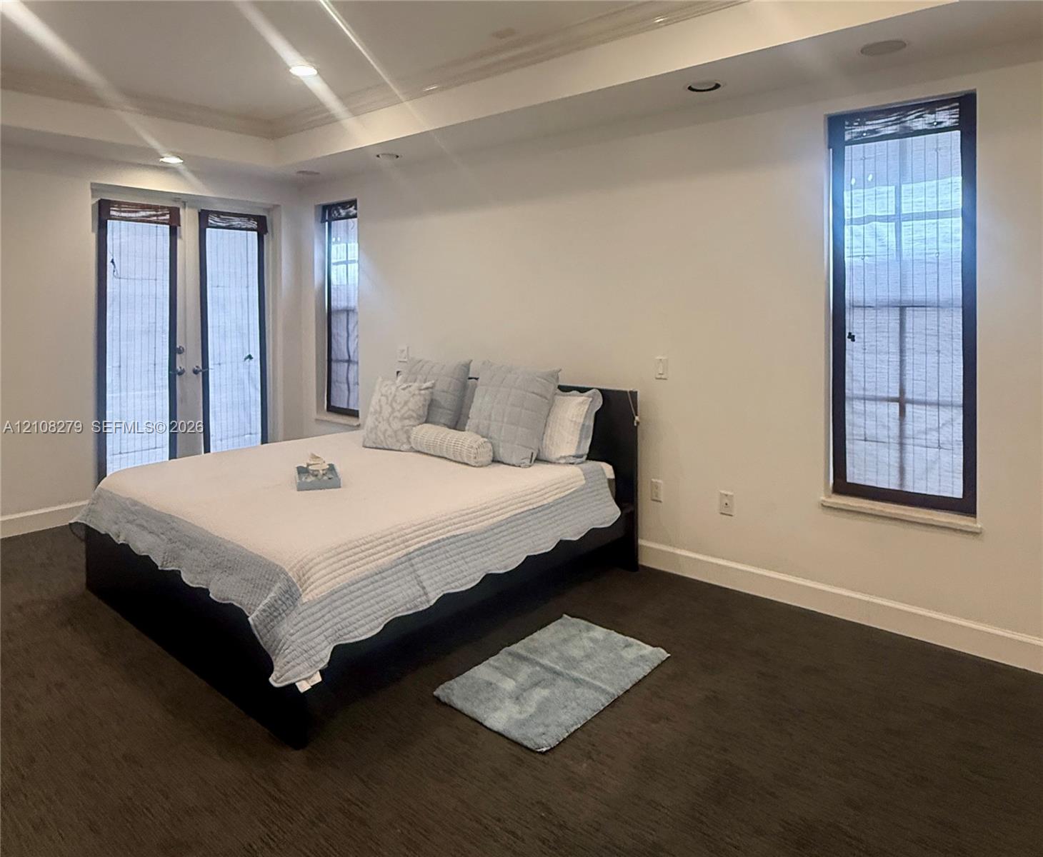 Room interior featuring dark carpeting, recessed ceiling lighting, tray ceiling architectural detail, tall windows, and glass-paned double doors