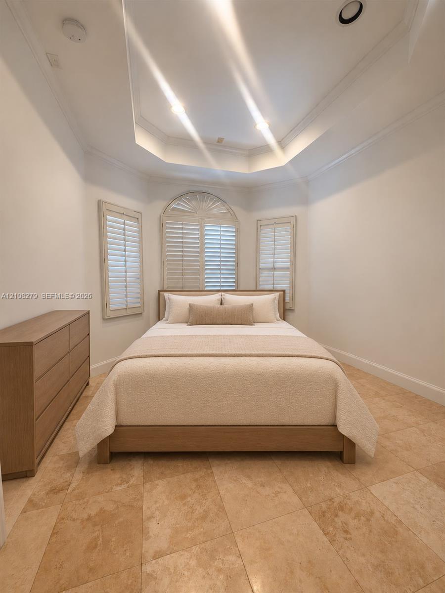 Tray ceiling featuring recessed lighting, stone tile flooring, and arched window with built-in interior shutters